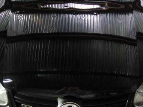 Czarny samochód z widocznymi śladami po gradobiciu na masce, widoczne wgniecenia i odbicia światła.