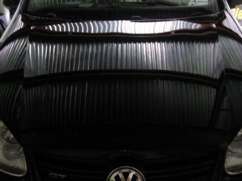 Błyszcząca maska czarnego samochodu marki Volkswagen po usunięciu wgnieceń, odbijająca światło w warsztacie w Raszczycach.