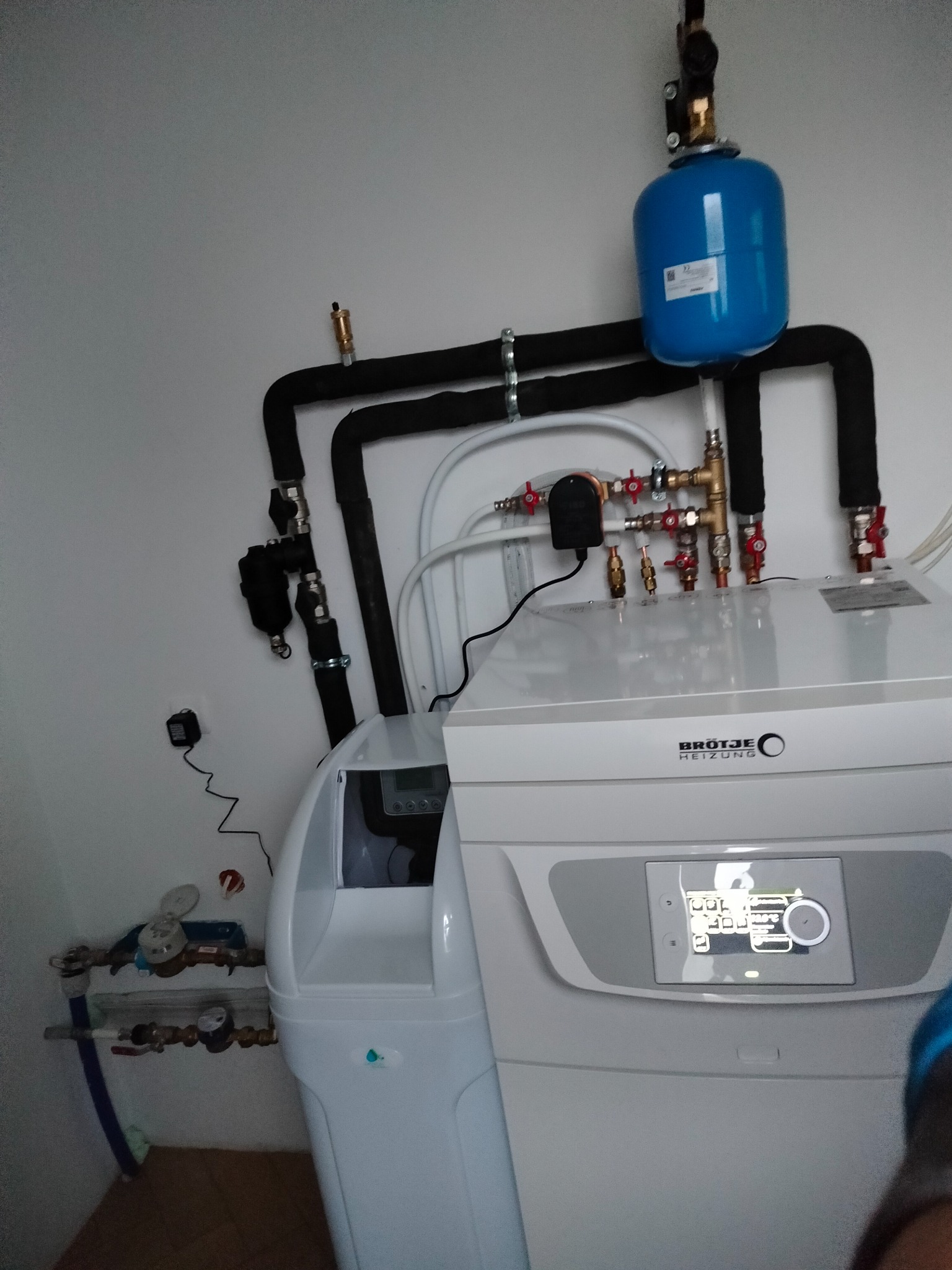 Nowoczesna instalacja grzewcza z białą jednostką centralną Brötje i niebieskim zbiornikiem wyrównawczym, rury w izolacji, widok instalacji hydraulicznej w Chocień.