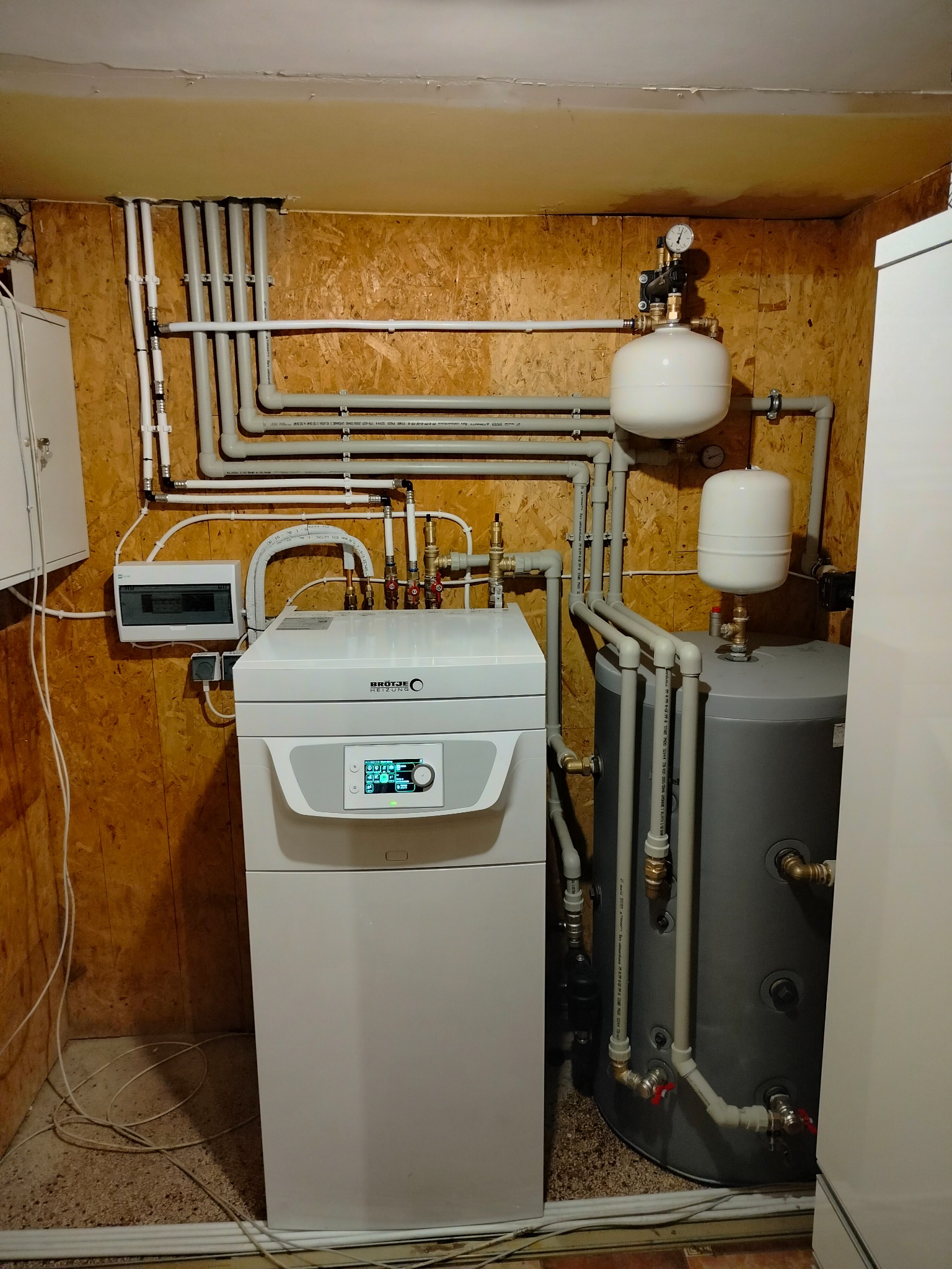 Kotłownia z piecem gazowym Brötje, zbiornikiem akumulacyjnym i rozbudowaną instalacją hydrauliczną z rur PCV na ścianach z boazerii.