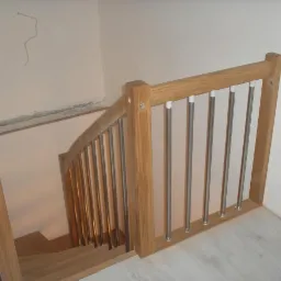 Drewniane schody z metalowymi balustradami, widok z góry. Jasne drewno, surowe ściany, biała podłoga. Element wykończenia wnętrza.