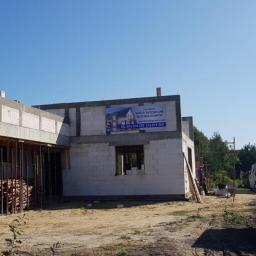 LECHDOM GARWOLIN - Budowa domu w trakcie: surowe ściany z betonu komórkowego, widoczne drewniane szalunki i zbrojenia. Na ścianie baner reklamowy firmy budowlanej. Przyczepka samochodowa w tle.