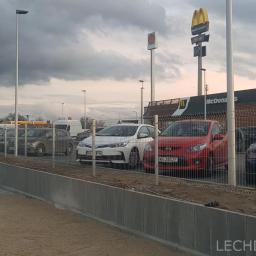LECHDOM GARWOLIN - Montaż obrzeży chodnikowych z szarej kostki betonowej przy parkingu McDonald's, widoczni dwaj pracownicy w odblaskowych kamizelkach i tarcze do cięcia betonu.