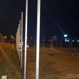 LECHDOM GARWOLIN - Montaż słupków ogrodzeniowych w nocy, widoczni pracownicy w odblaskowych ubraniach, w tle oświetlona droga i reklamy.