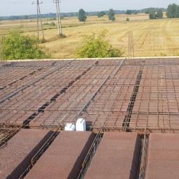 LECHDOM GARWOLIN - Zbrojenie stropu Teriva na budowie domu jednorodzinnego, widok z góry na ułożone bloczki i siatkę z prętów stalowych, wystające pionowe pręty, w tle pole i drzewa.
