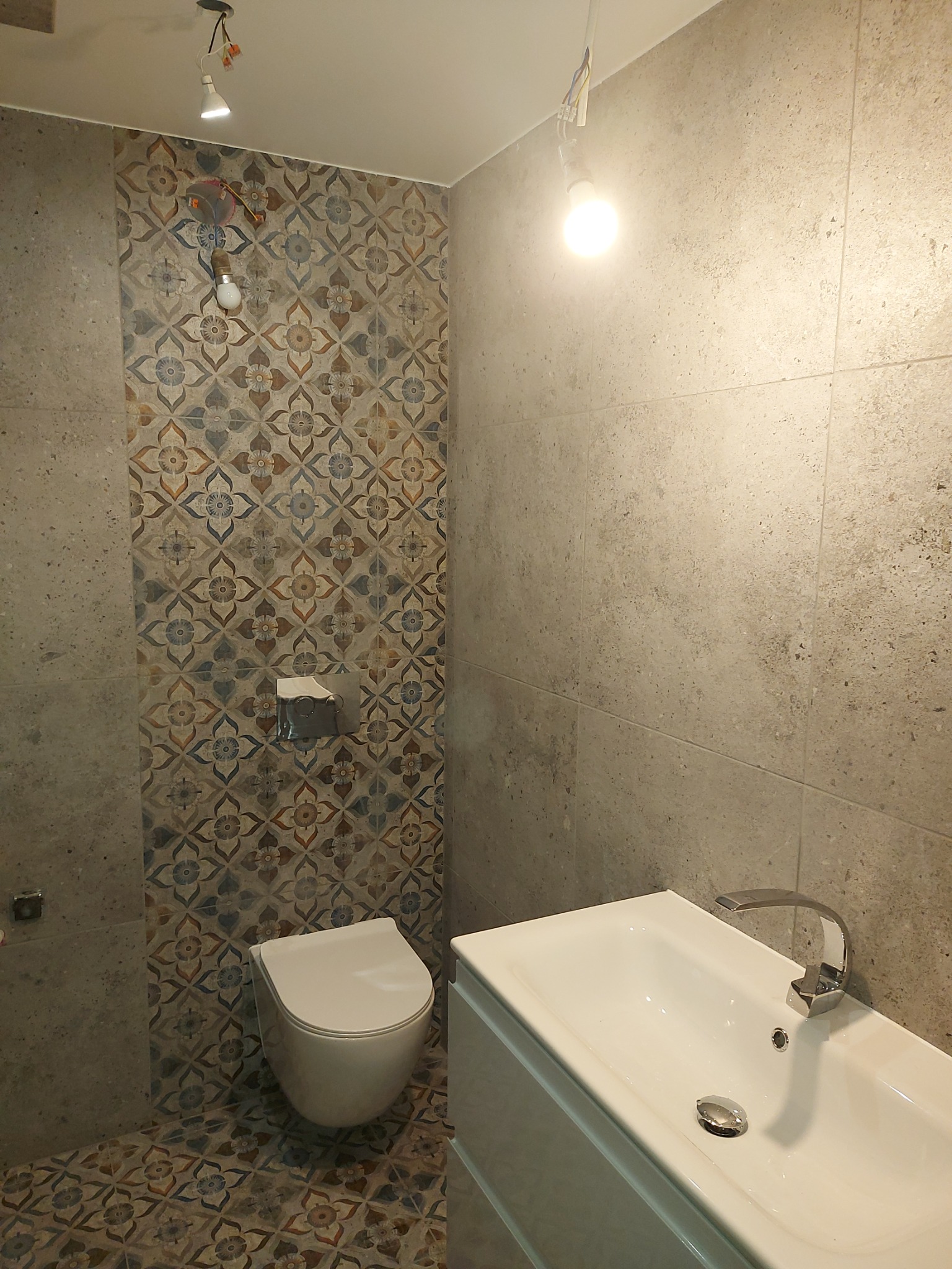 Nowoczesna łazienka z wiszącą toaletą, umywalką nablatową i płytkami w stylu patchwork na ścianie i podłodze, oświetlenie punktowe.