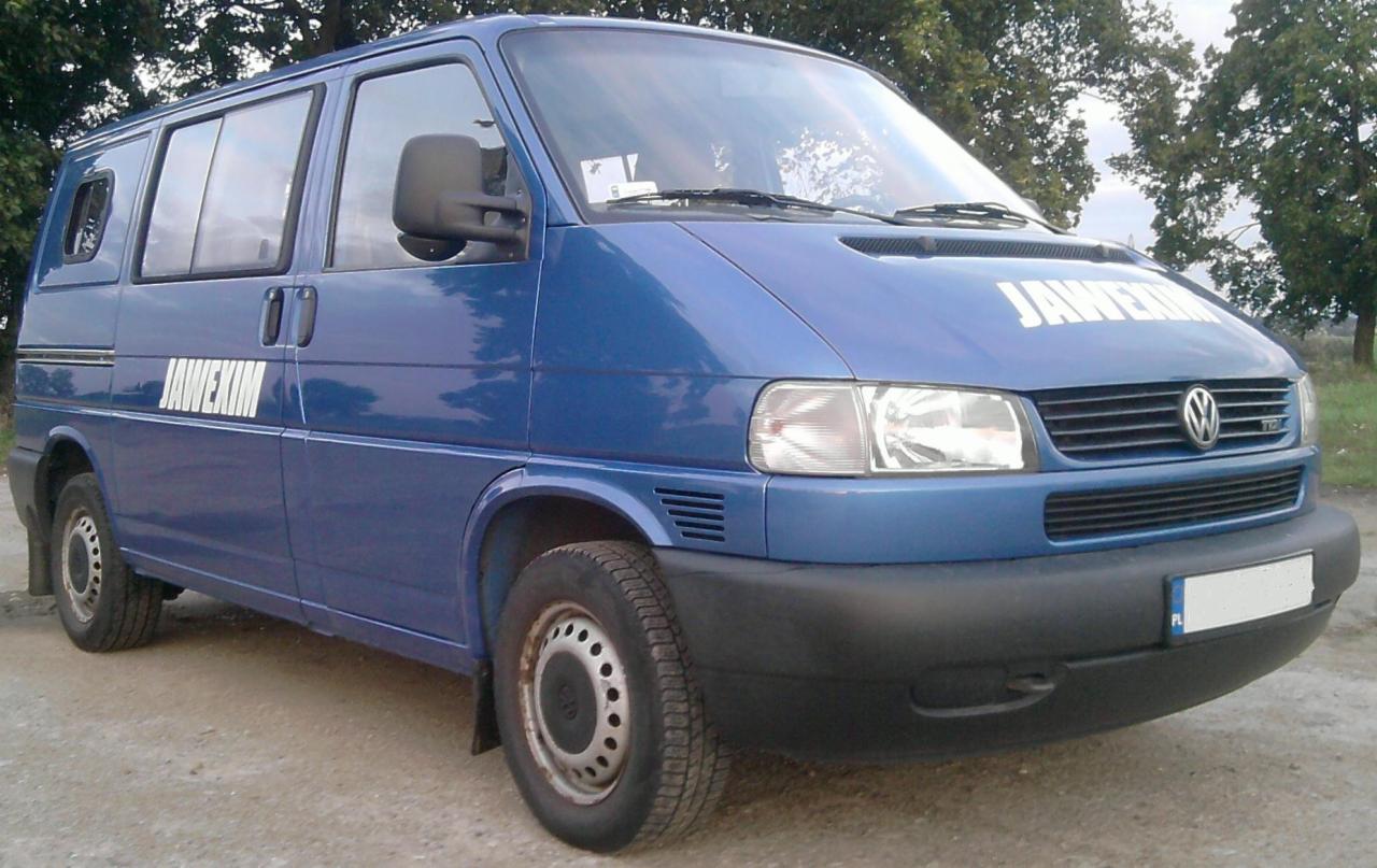 Niebieski bus Volkswagen Transporter z napisem 'JAWEXIM' na boku i masce, zaparkowany na szutrowej drodze, z widocznymi drzewami w tle.