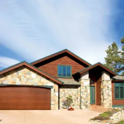 Dom jednorodzinny z kamienną elewacją i brązową bramą garażową segmentową, widoczny z przodu, z bonsai w doniczce przed wejściem.