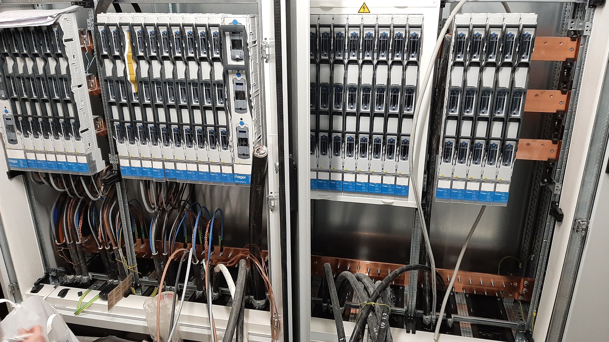 Rozdzielnia elektryczna z zamontowanymi modułowymi wyłącznikami nadprądowymi firmy Hager, widoczne kable i szyny zbiorcze.