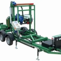 Mobilny, zielony traktor z piłą taśmową do cięcia drewna, z panelem sterowania i silnikiem, gotowy do transportu na przyczepie.