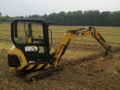 Żółto-czarna minikoparka CAT 301.5 w trakcie prac ziemnych na polu, widoczne świeżo przekopane bruzdy w ziemi.