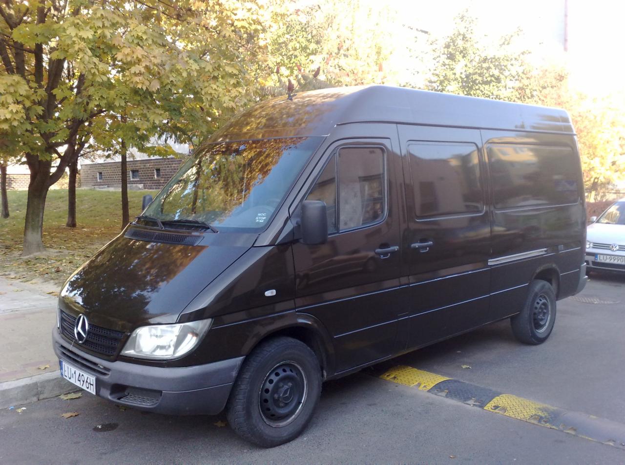 Ciemny bus Mercedes-Benz zaparkowany na ulicy z żółto-czarnym progiem zwalniającym, jesienne drzewa w tle.