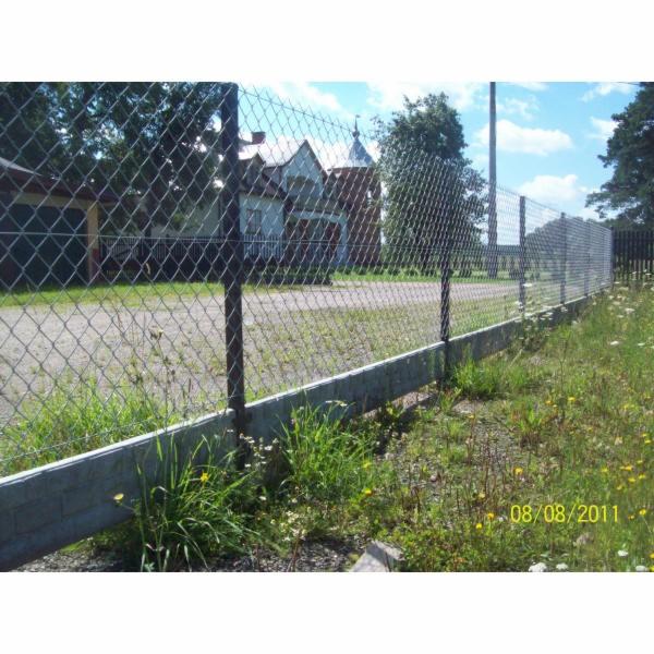 Ogrodzenie z siatki plecionej na betonowej podmurówce, widok z zewnątrz, w tle budynek z wieżyczką, data na zdjęciu 08/08/2011.