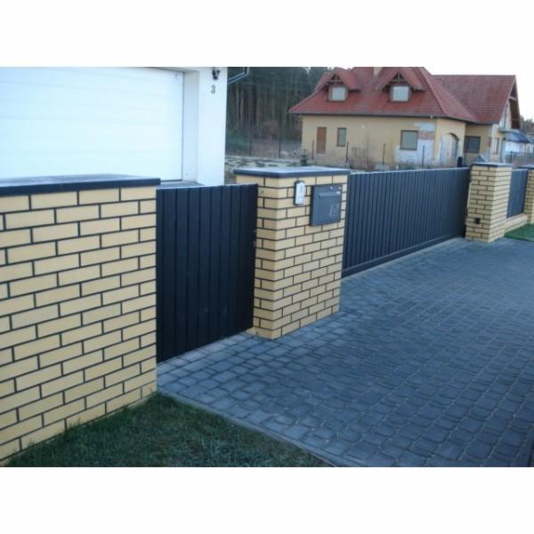 Ogrodzenie posesji z przesuwną bramą, słupki z jasnej cegły klinkierowej, czarna metalowa brama i furtka, szara kostka brukowa na podjeździe, dom jednorodzinny w tle.