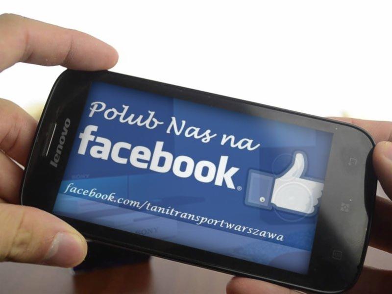 Smartfon Lenovo z wyświetlonym zaproszeniem do polubienia profilu firmy Tanitransportwarszawa na Facebooku. Widoczna dłoń trzymająca urządzenie.