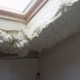 Ocieplenie poddasza pianką PUR wok&oacute;ł okna dachowego, widoczne nier&oacute;wności i struktura pianki. Detal wykończenia izolacji natryskowej w trudno dostępnym miejscu.