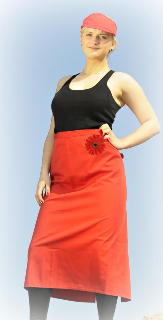 Kobieta w czarnym topie i czerwonej spódnicy z aplikacją kwiatową, stojąca na tle nieba.