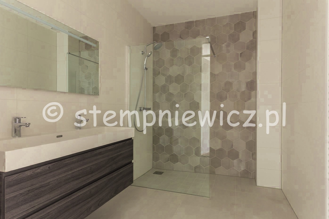 Nowoczesna łazienka z kabiną prysznicową typu walk-in, heksagonalnymi płytkami w odcieniach szarości na ścianie i umywalką nablatową z szafką z ciemnego drewna.