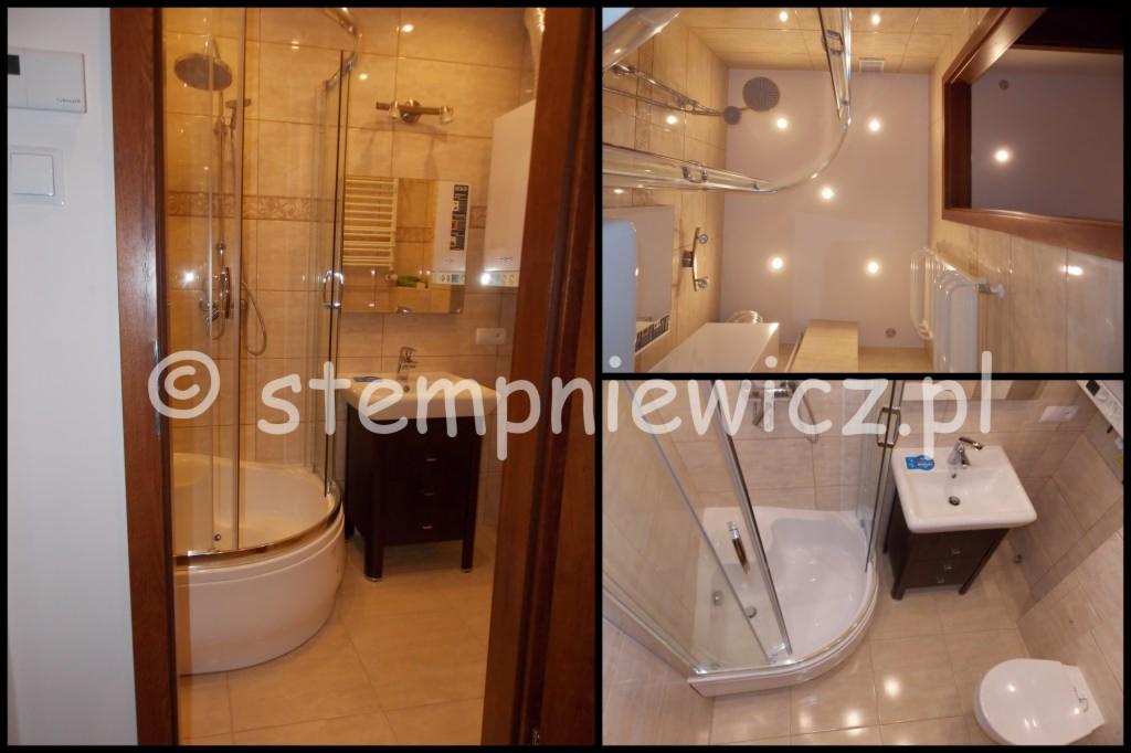 Wykończona łazienka z kabiną prysznicową półokrągłą, umywalką z szafką w kolorze ciemnego brązu i beżowymi płytkami na ścianach oraz podłodze, z widocznym bojlerem na ścianie.