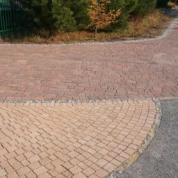 Kaskadowe przejście z czerwonej kostki brukowej w łuk z jasnej kostki, obramowane szarą kostką granitową, tworzące ścieżkę w ogrodzie.