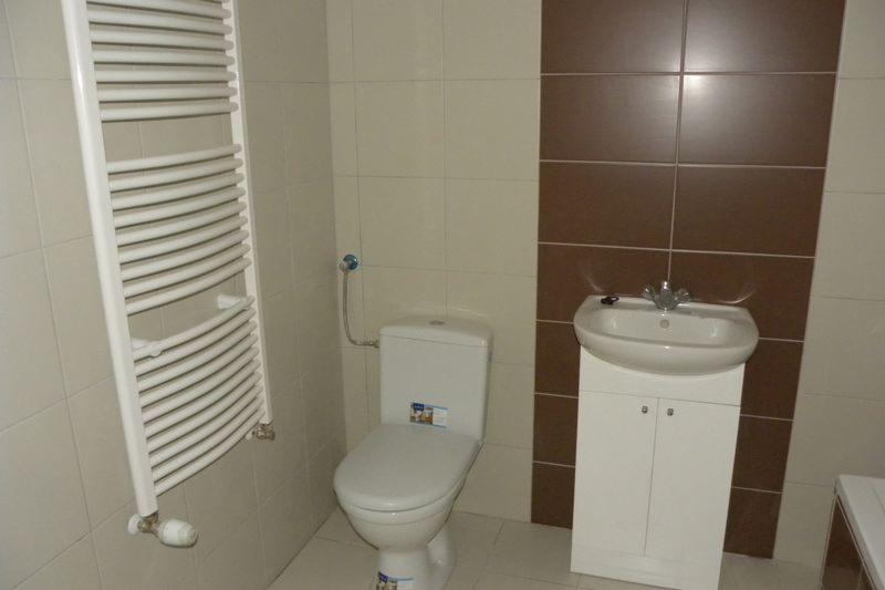 Wykończona łazienka z beżowymi i brązowymi płytkami, białą toaletą, umywalką z szafką i grzejnikiem drabinkowym.