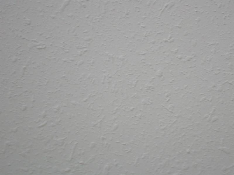 Szara ściana pokryta tynkiem strukturalnym o wyraźnej fakturze, zbliżenie na nierówną powierzchnię.