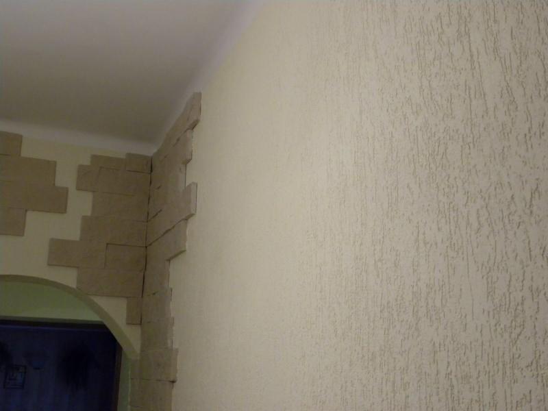 Wykończenie ściany tynkiem strukturalnym i dekoracyjnym kamieniem wokół łuku drzwiowego w Turze. Widoczna faktura tynku mineralnego.