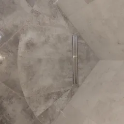 Szare płytki podłogowe ułożone w geometryczny wzór z liniowym odpływem w kabinie prysznicowej.