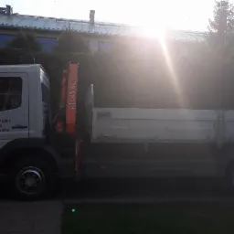 Biała ciężarówka z dźwigiem Atlas 60.1 na tle budynku z metalowym dachem, widoczne numery kontaktowe na kabinie.