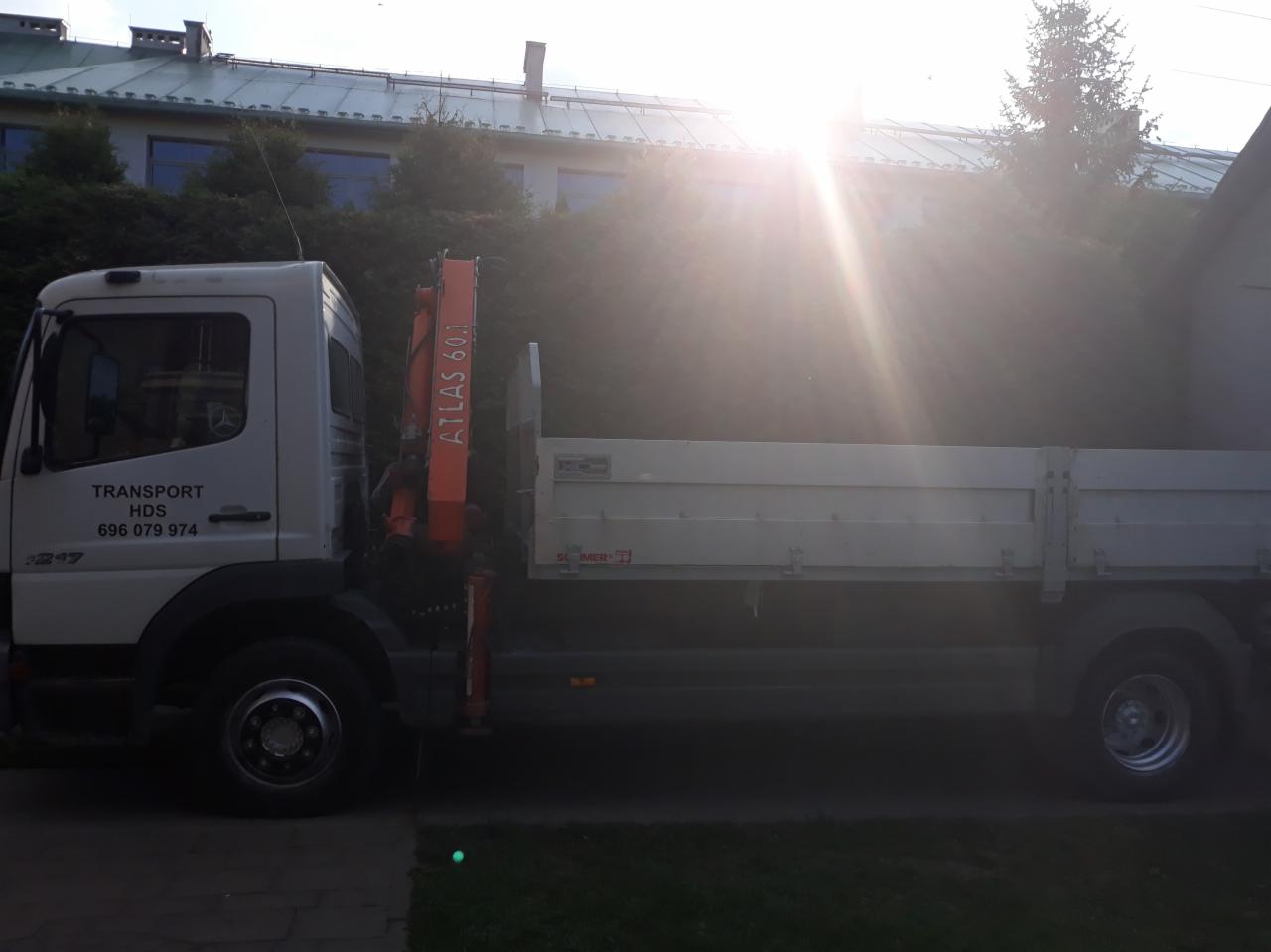 Biała ciężarówka z dźwigiem Atlas 60.1 na tle budynku z metalowym dachem, widoczne numery kontaktowe na kabinie.