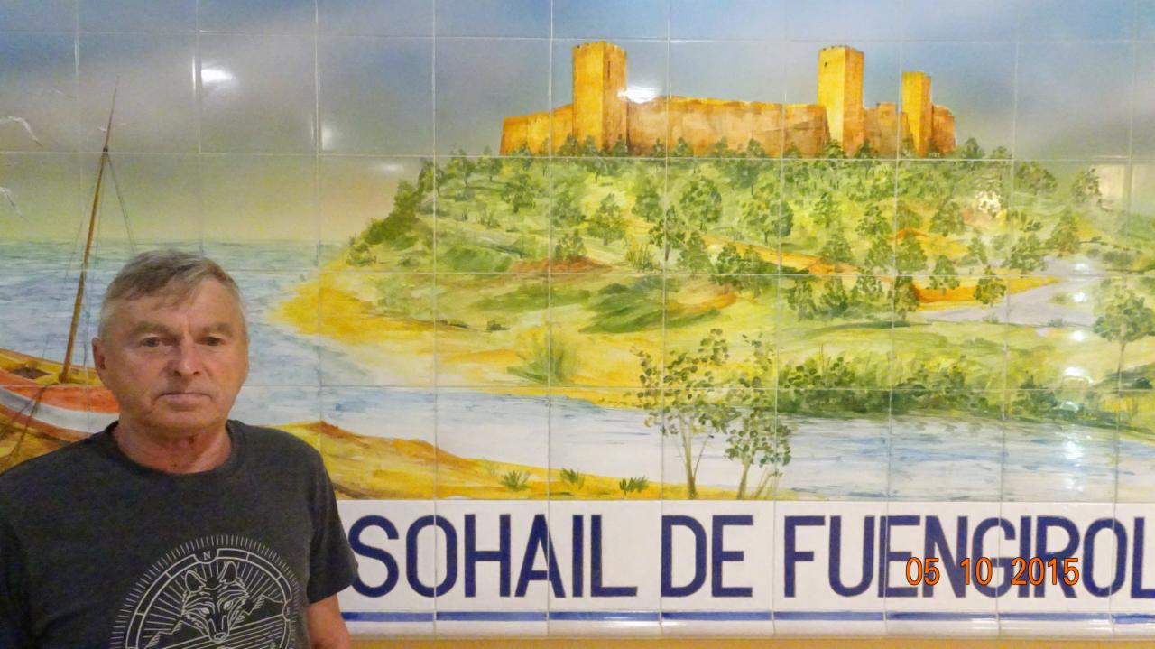 Mężczyzna pozuje na tle ceramicznej mozaiki przedstawiającej zamek Sohail w Fuengirola, Hiszpania, z datą 05 10 2015