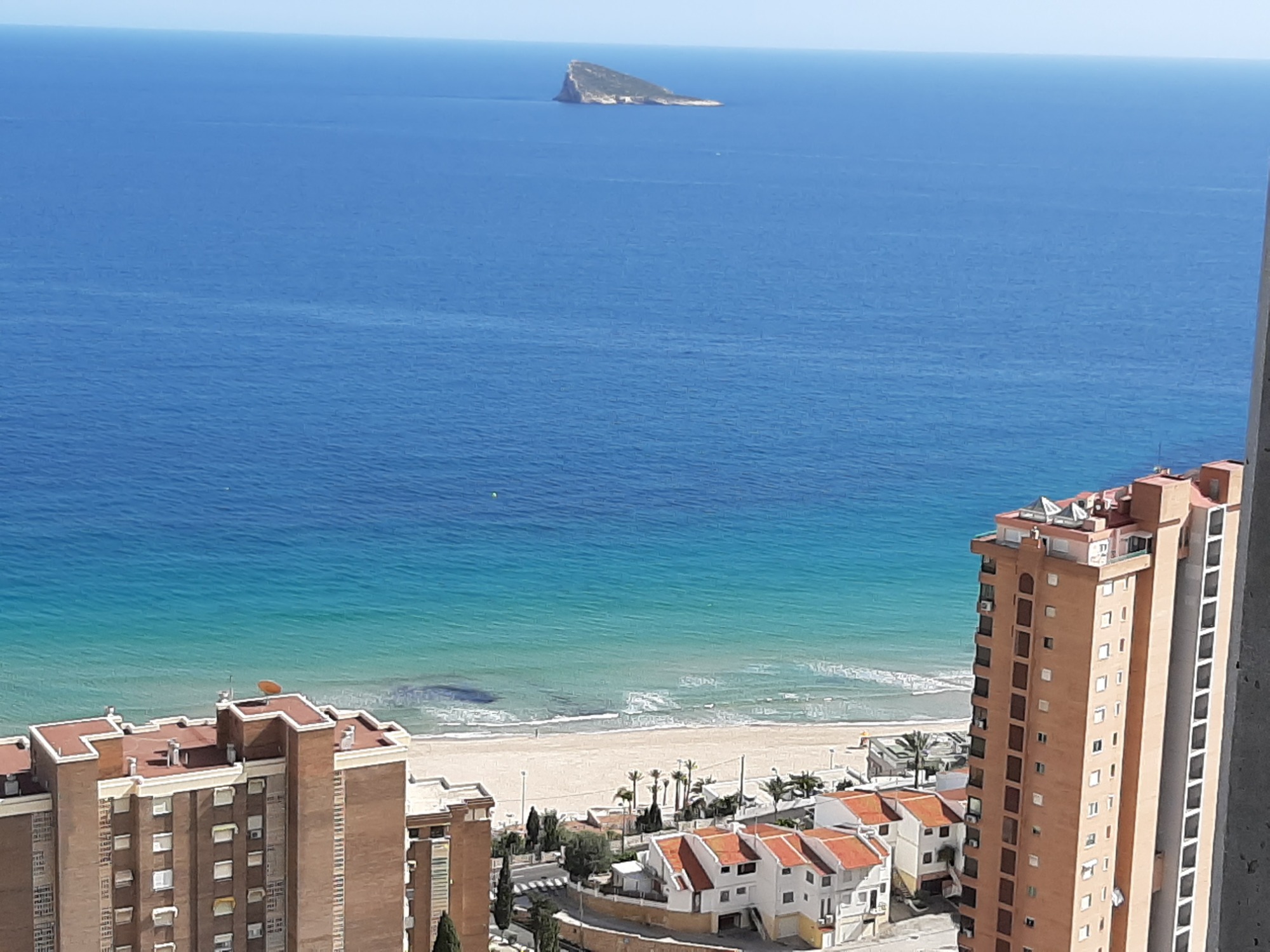 Widok z wysokości na plażę w Benidormie, Costa Blanca, z budynkami apartamentowymi w pierwszym planie i wyspą na horyzoncie.