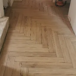 Ułożona podłoga z paneli w jodełkę w trakcie remontu, widoczne niedokończone ściany i przewody elektryczne.