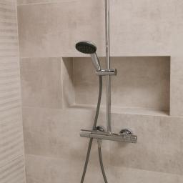 Certa-Bud - Nowoczesna kabina prysznicowa z chromowaną armaturą i deszczownicą, beżowe płytki imitujące kamień, wnęka w ścianie.