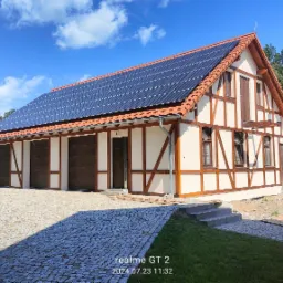 Budynek w stylu szachulcowym z panelami słonecznymi na dachu, widok z brukowanego podjazdu, błękitne niebo w tle.