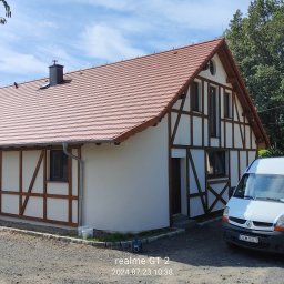 OCIEPLENIA, ELEWACJE KOMPLEKSOWO - Budynek z elewacją w stylu szachulcowym, świeżo po malowaniu, z zaparkowanym białym vanem i pracującym mężczyzną przy klimatyzatorze na zewnątrz.