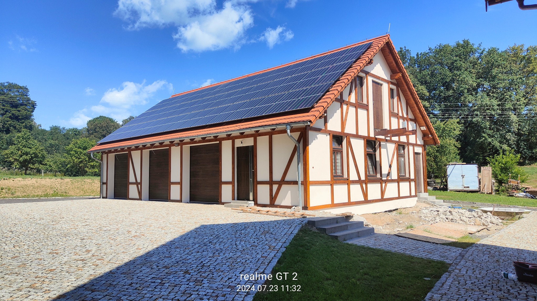 Budynek w stylu szachulcowym z panelami słonecznymi na dachu, widok z brukowanego podjazdu, błękitne niebo w tle.