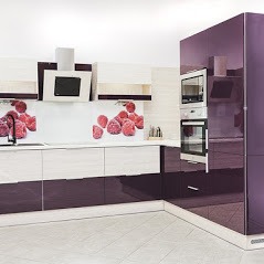 Nowoczesna kuchnia w odcieniach fioletu i kremu, z błyszczącymi frontami szafek i panelem szklanym z motywem malin. Widoczny okap, piekarnik i mikrofalówka w zabudowie.