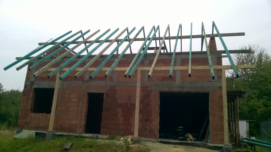 Budowa domu z czerwonej cegły w Pałecznicy na etapie wznoszenia ścian i montażu drewnianej konstrukcji dachu z zielonymi elementami impregnacyjnymi.