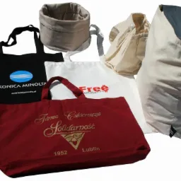 Zestaw różnorodnych toreb materiałowych z nadrukami firmowymi, w tym bordowa torba z napisem 'Firma Cukiernicza Solidarność Lublin 1952' i czarna torba z logo Konica Minolta.