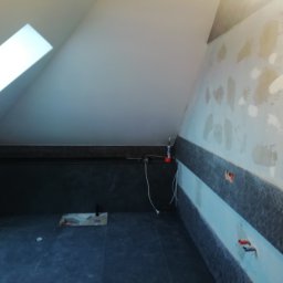 Flis Servis - Łazienka na poddaszu w trakcie remontu: częściowo położone ciemne płytki na podłodze i ścianie, ściany przygotowane pod malowanie, widoczne kable elektryczne.