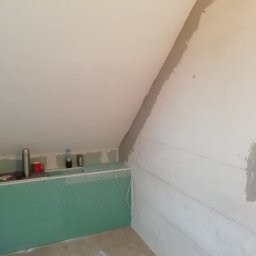 Flis Servis - Ścianka działowa z płyt gipsowo-kartonowych w trakcie budowy w Twardogórze, widoczne przewody elektryczne i przygotowane punkty instalacyjne, na górze ścianki leżą butelki z wodą i termos.