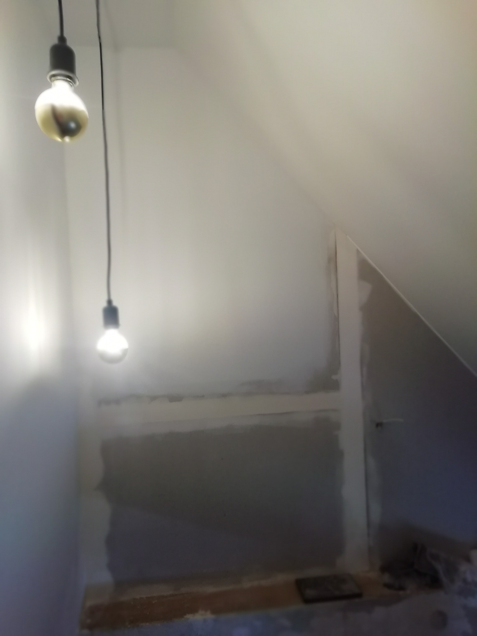 Poddasze w trakcie remontu, ściany przygotowane do malowania, widoczne dwie wiszące żarówki bez kloszy.