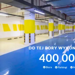 Błękitna posadzka w hali garażowej z żółtymi akcentami na kolumnach i ścianach, zabezpieczenia na słupach, widok na puste stanowiska parkingowe.