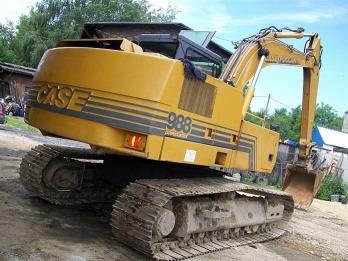 Żółta koparka gąsienicowa CASE 988 na placu budowy, widok z boku, z widocznymi elementami konstrukcyjnymi i oponami gąsienicowymi.