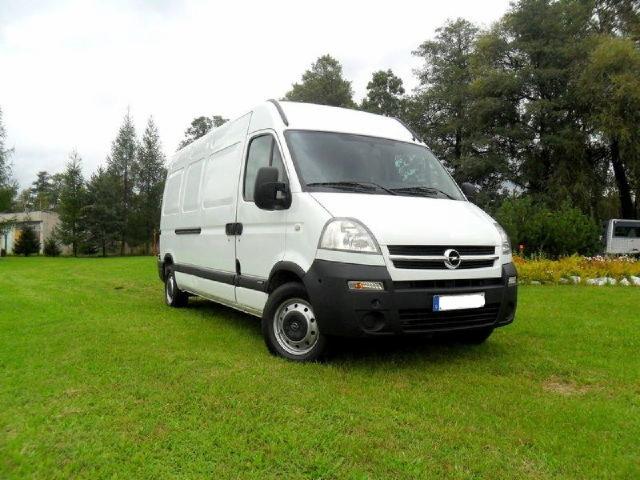 Biały Opel Movano na trawniku, z widocznym fragmentem budynku w tle, sfotografowany pod lekkim kątem z przodu.