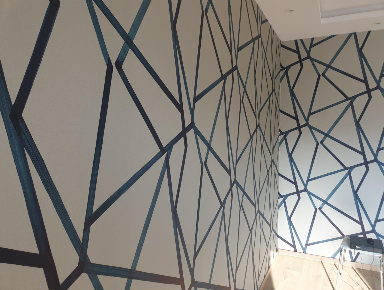 Pokój po tapetowaniu z geometrycznym wzorem w odcieniach błękitu. Widok na narożnik, podkreślający precyzję wykonania. Jasne panele podłogowe.