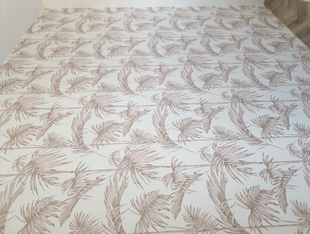 Ściana pokryta jasną tapetą w motywie palmowych liści z efektem drewnianych desek w tle.