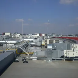 Rozbudowana instalacja wentylacyjna i klimatyzacyjna na dachu budynku komercyjnego z widocznymi przewodami wentylacyjnymi, klimatyzatorami, schodami technicznymi i zabezpieczeniami odgromowymi.