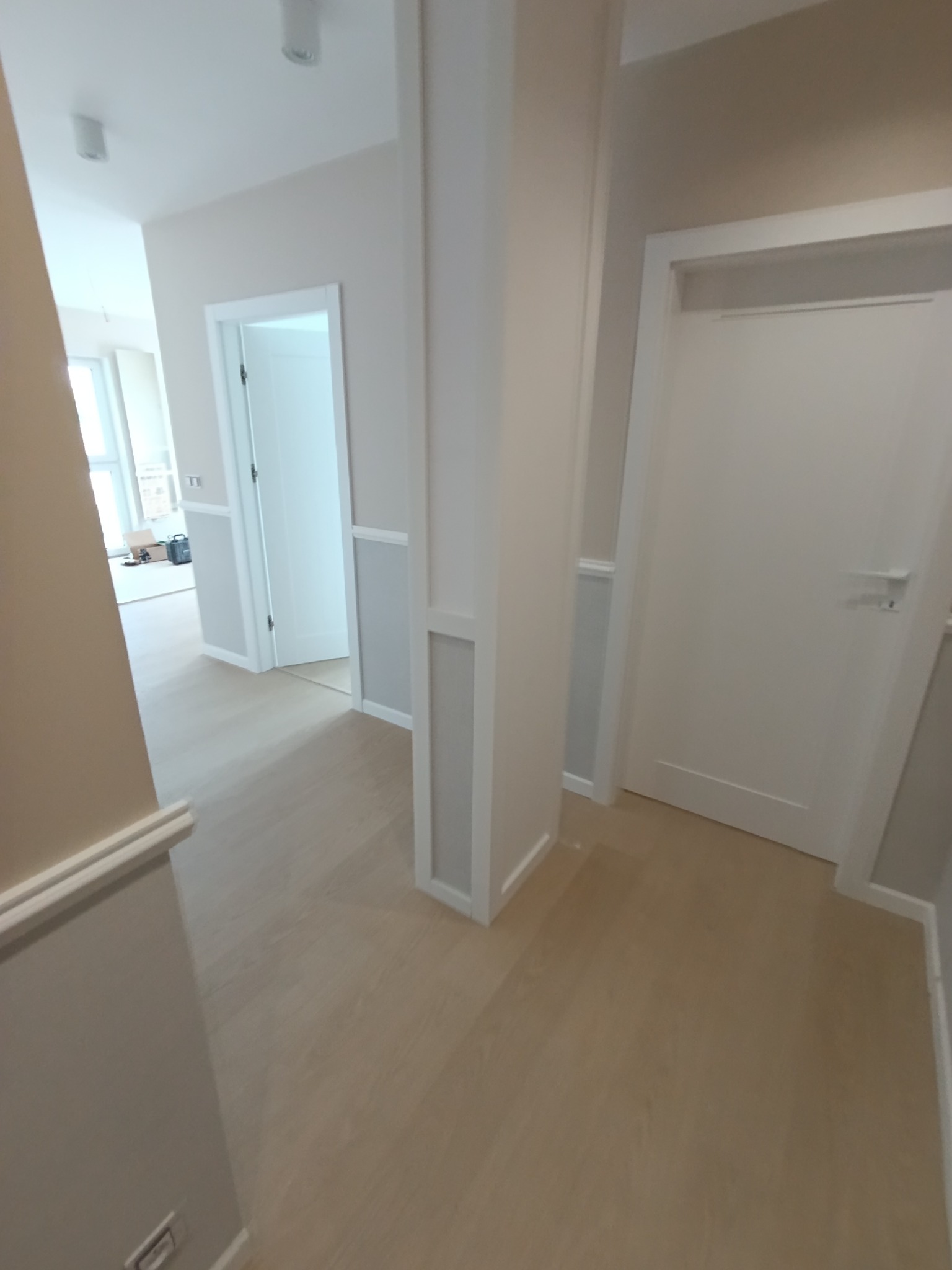 Jasny korytarz po remoncie z drewnianą podłogą, białą stolarką drzwiową i dekoracyjnymi panelami ściennymi w odcieniach bieli i szarości.